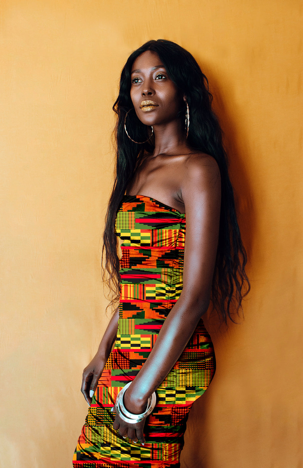 Woman wearing a colorful African Kente patterned dress against an orange background
