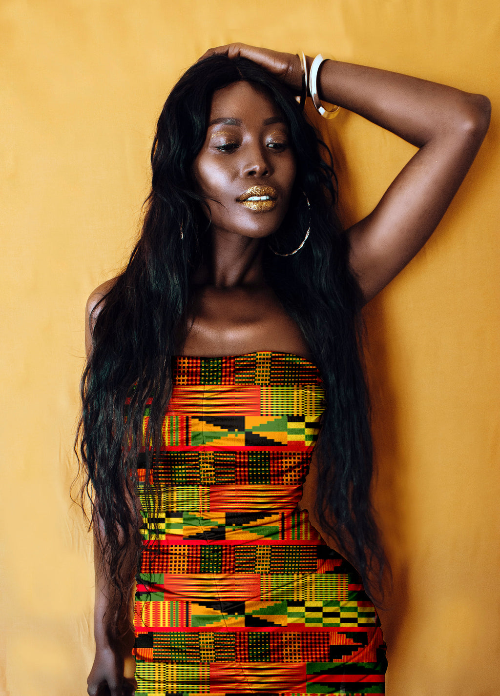 Woman wearing a colorful African Kente patterned dress against a yellow background
